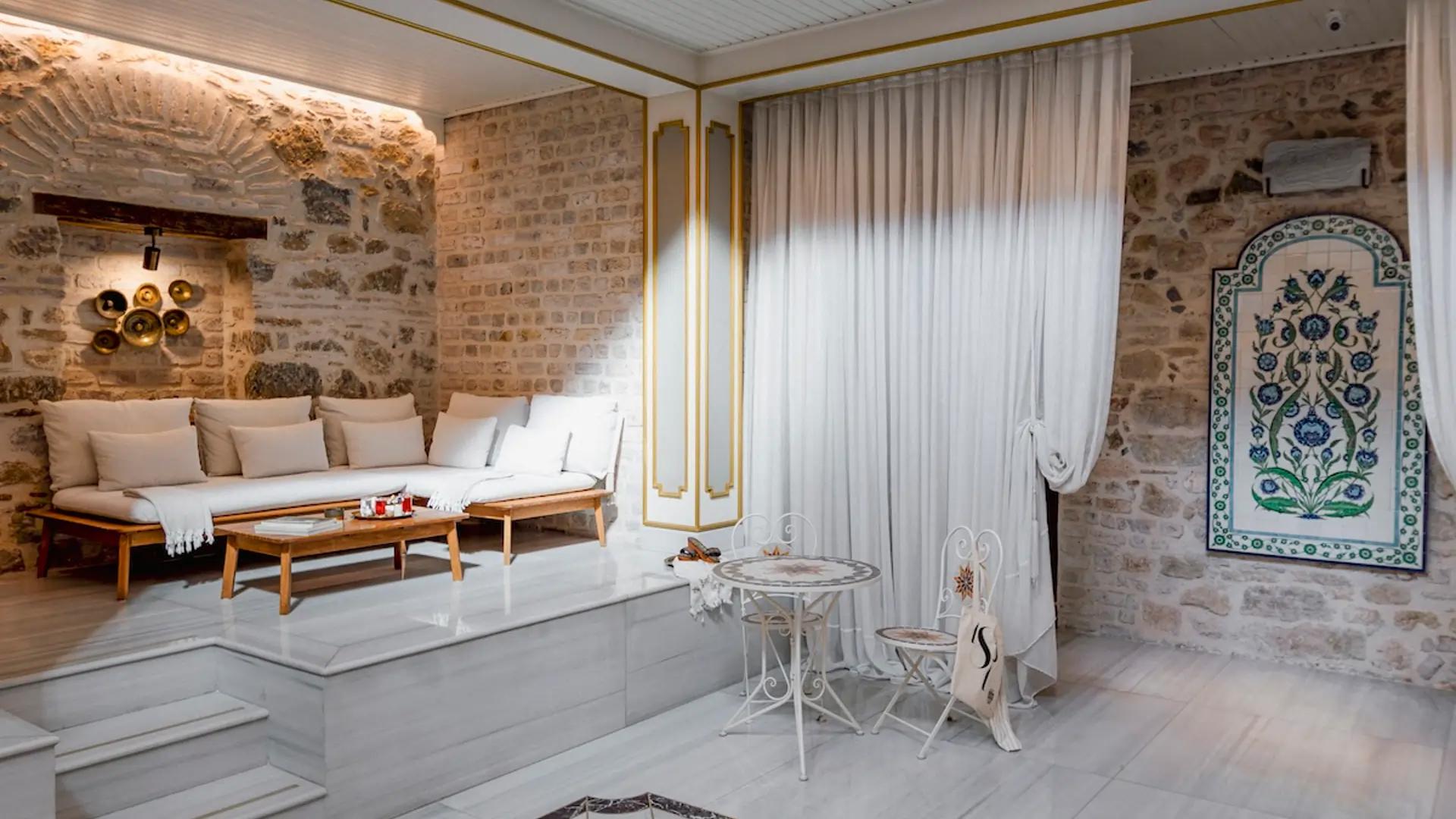 A tranquil space with white furniture and a stone wall, capturing the historical charm of the Cukurcuma Hammam experience