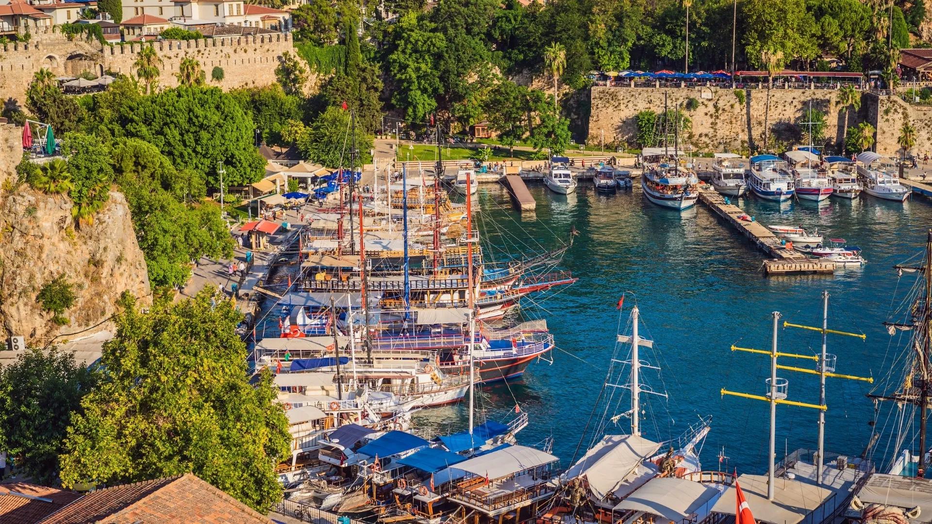 Panoramic view of Antalya Old Harbor with traditional boats, ancient city walls, and Mediterranean scenery.