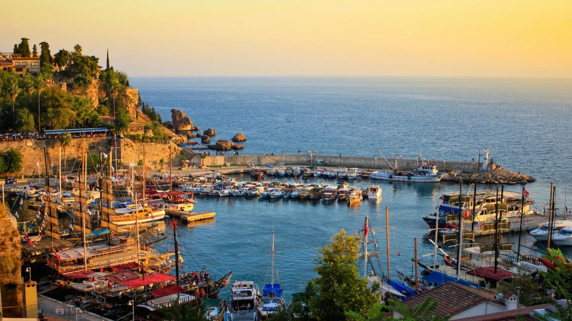 Sunset view over Antalya Old Harbor, with wooden boats, coastal cliffs, and peaceful Mediterranean atmosphere.