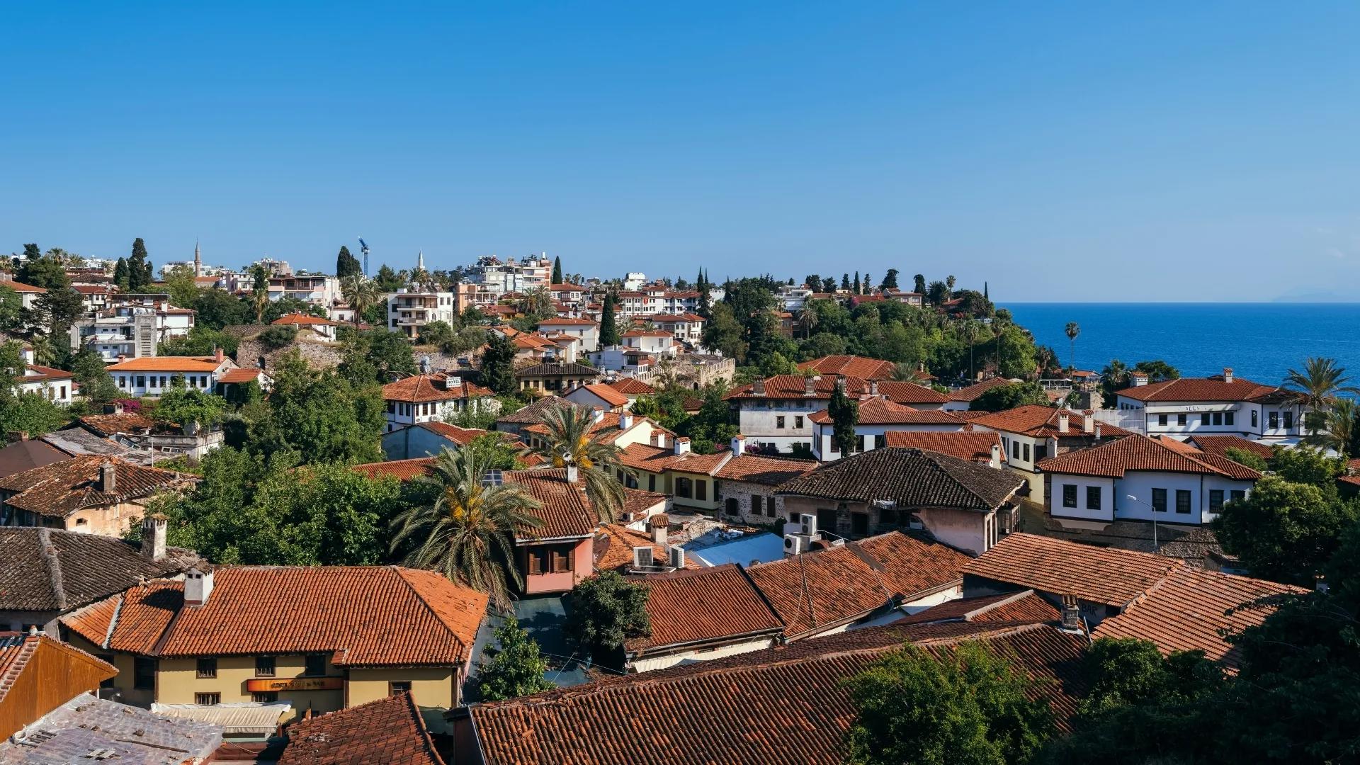 Scenic view of Antalya Old Town rooftops, traditional houses, green hills, and the Mediterranean Sea.